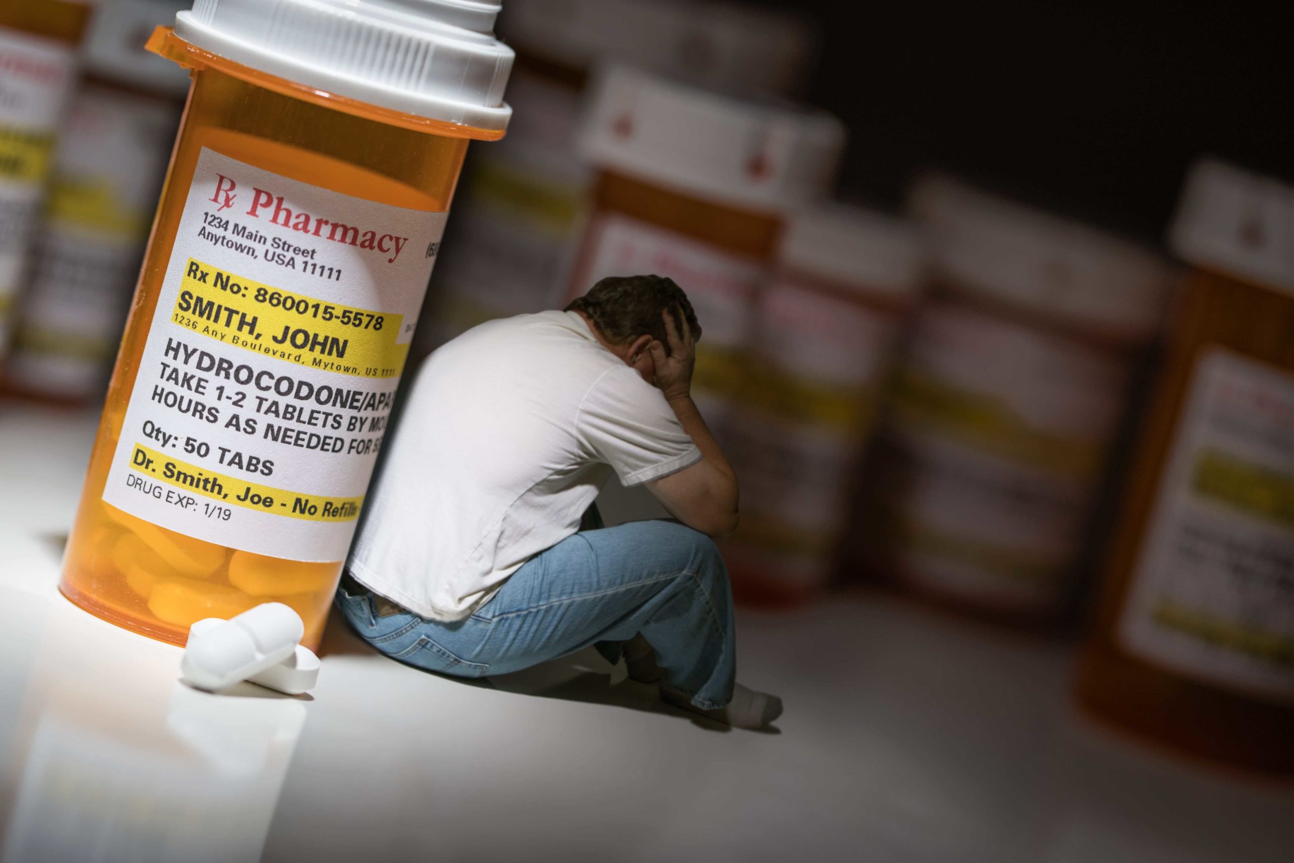 man sitting next to prescription pill bottles depicting addiction